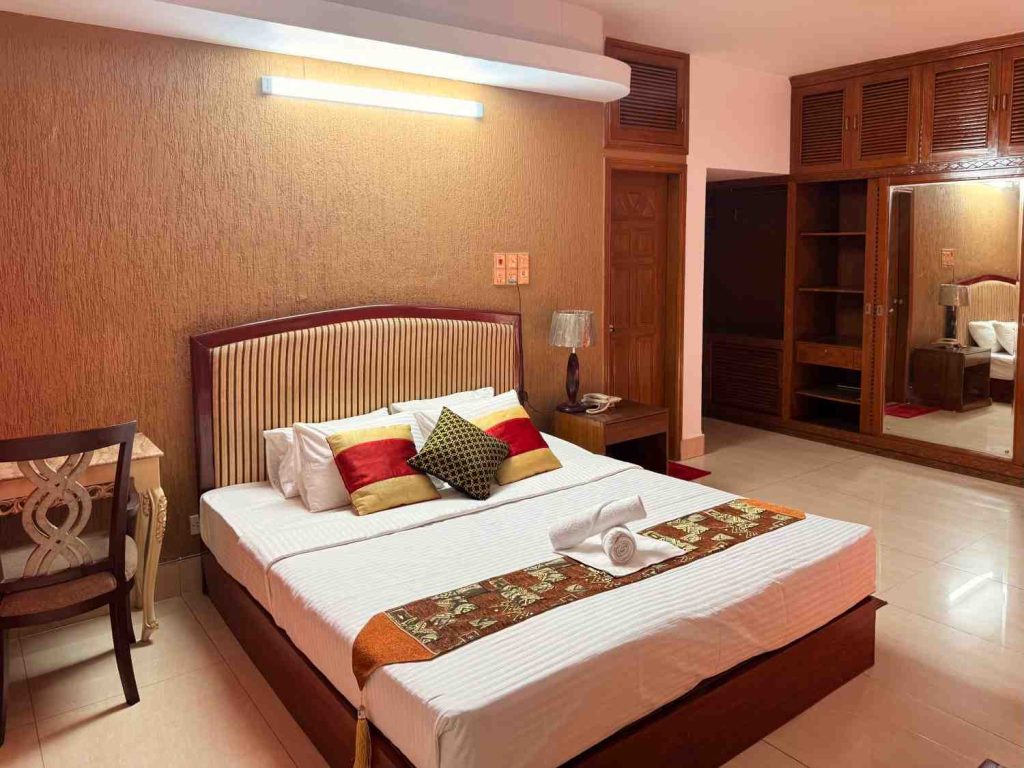 Elegant hotel bedroom with stylish decor, striped bed, pillows, and wardrobe in Bangladesh.